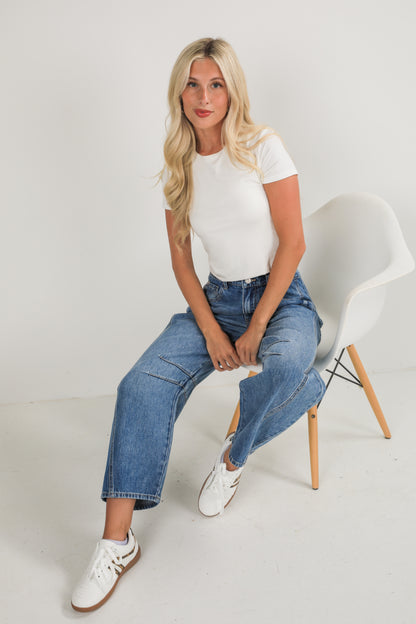 Woman sitting on a white chair wearing a white t-shirt and blue jeans.