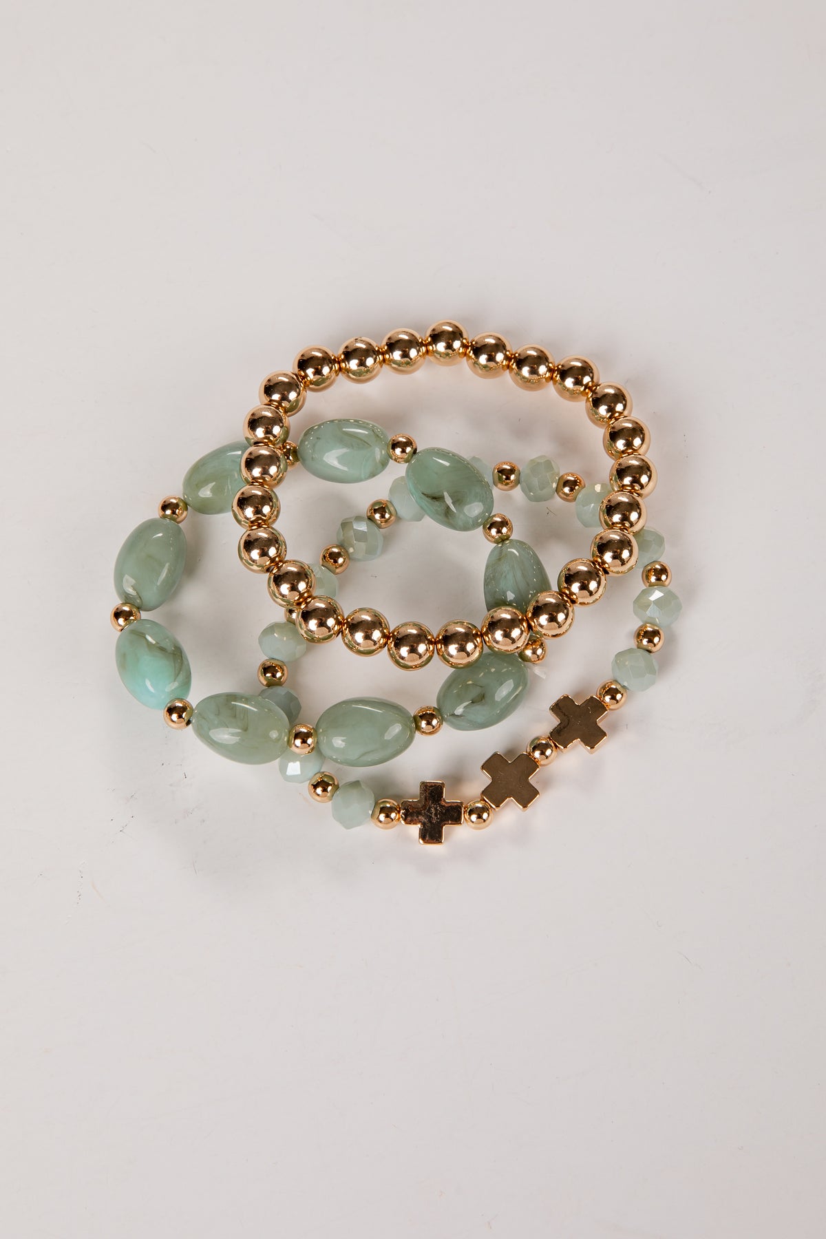 three bracelets with green beads and gold accents on a light gray background