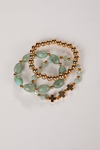 three bracelets with green beads and gold accents on a light gray background