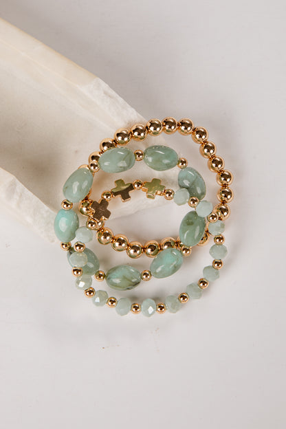 three bracelets with green beads and gold accents on a light gray background