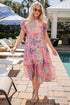 Woman in a colorful dress standing by a poolside with lounge chairs and umbrellas.