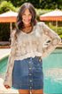 Woman wearing a lace top and denim skirt by a poolside with orange umbrellas in the background.