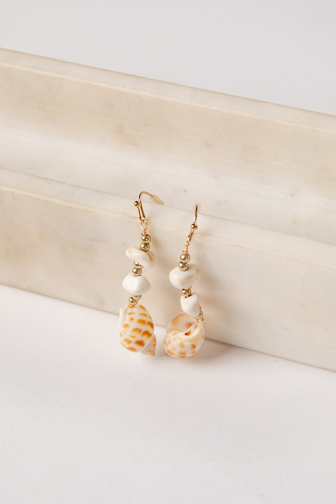 Shell and pearl earrings on a textured beige surface