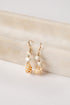 Shell and pearl earrings on a textured beige surface