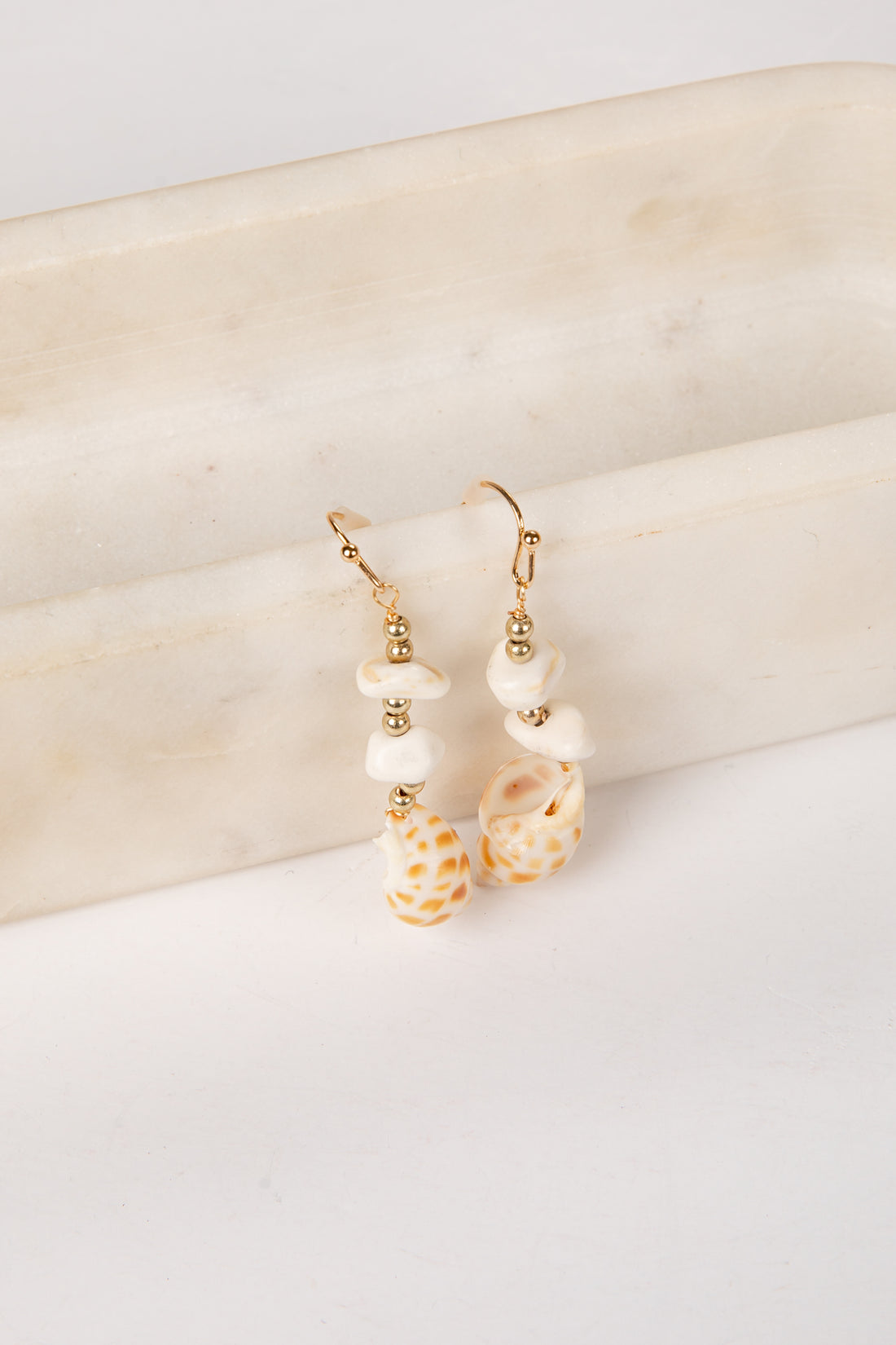 Pair of earrings with shell and pearl details on a light background