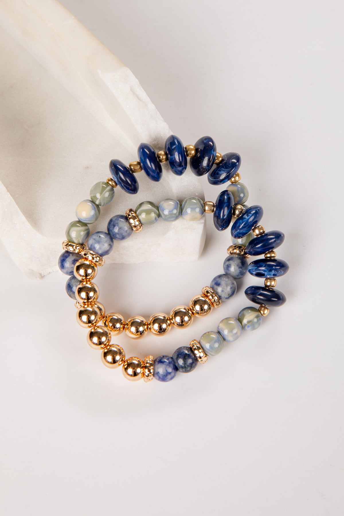 Set of three beaded bracelets with blue, gold, and gray beads on a white surface.