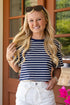 Woman wearing a striped shirt and white pants standing in front of a door with a blurred background