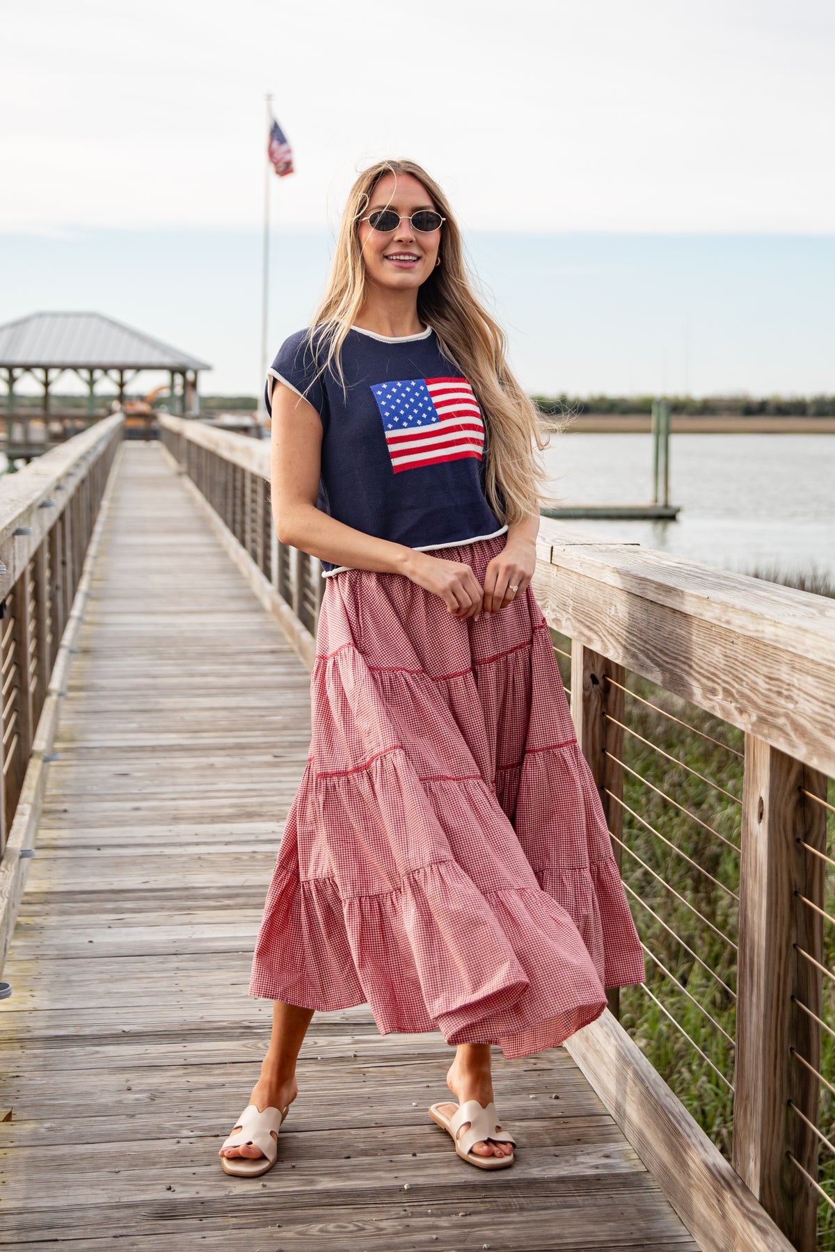 Woman wearing a navy t-shirt with an American flag and a pink skirt on a wooden dock.