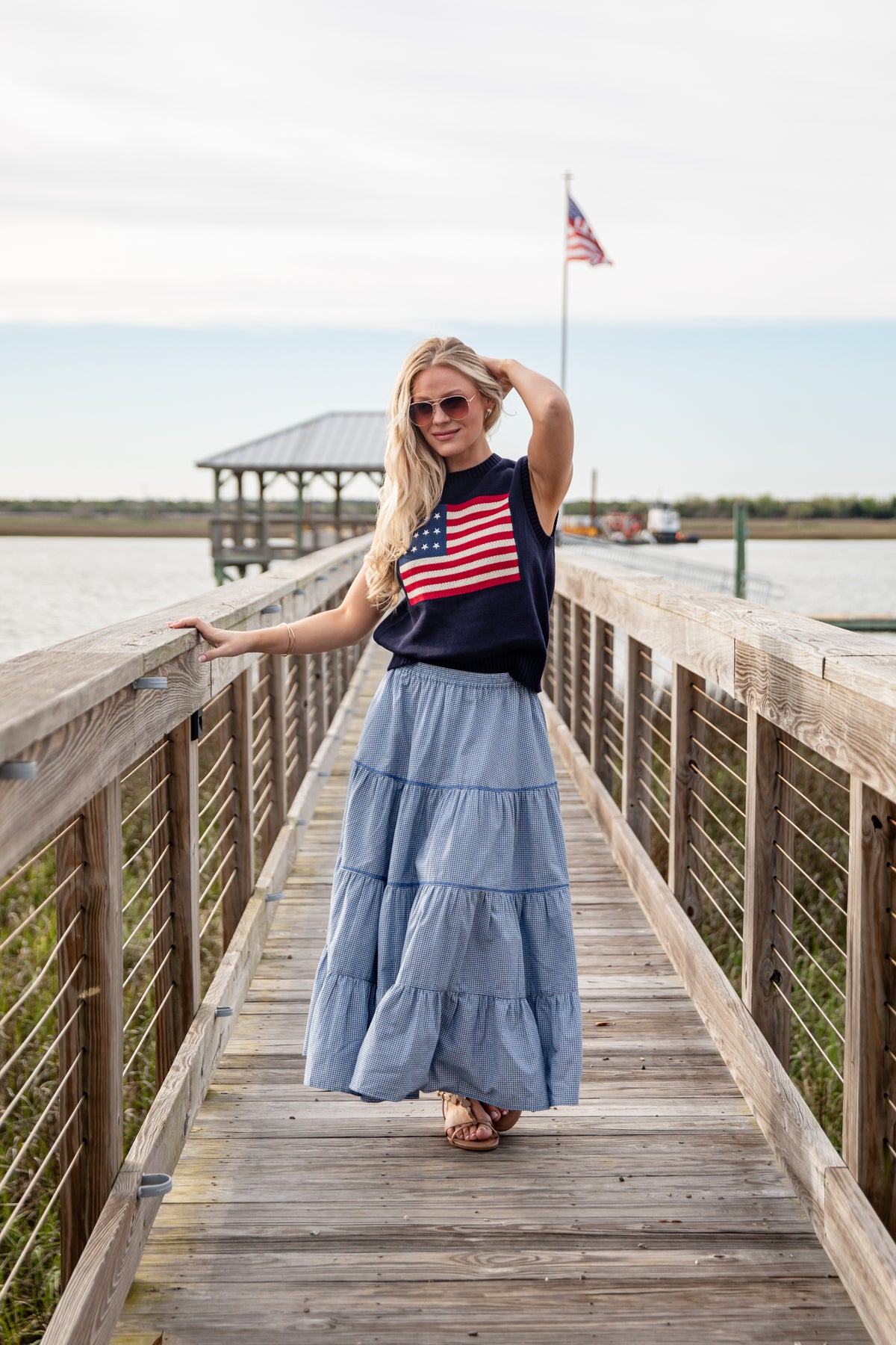 Woman standing on a wooden boardwalk wearing an American flag shirt and blue skirt.