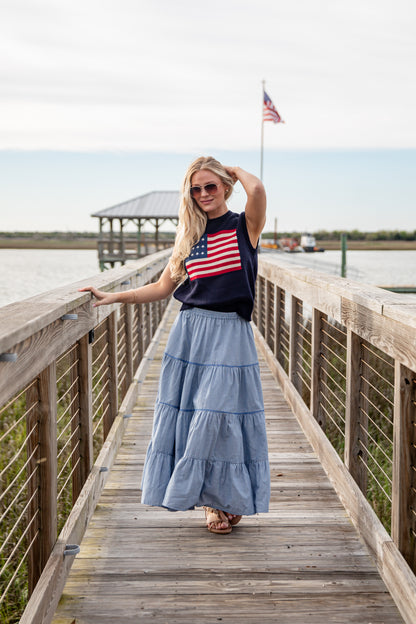 Woman standing on a wooden boardwalk wearing an American flag shirt and blue skirt.
