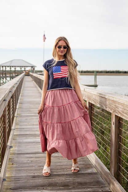 Woman wearing a navy t-shirt with an American flag design and a pink skirt on a wooden dock.