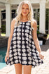 Woman wearing a black dress with white shell pattern by a poolside.