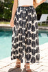 Person wearing a white top and black and white patterned pants by a pool.
