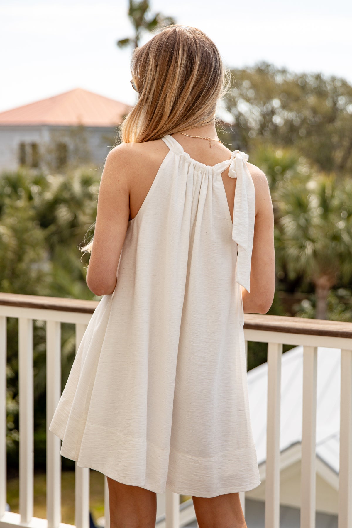 Woman in a white dress standing on a balcony with greenery in the background