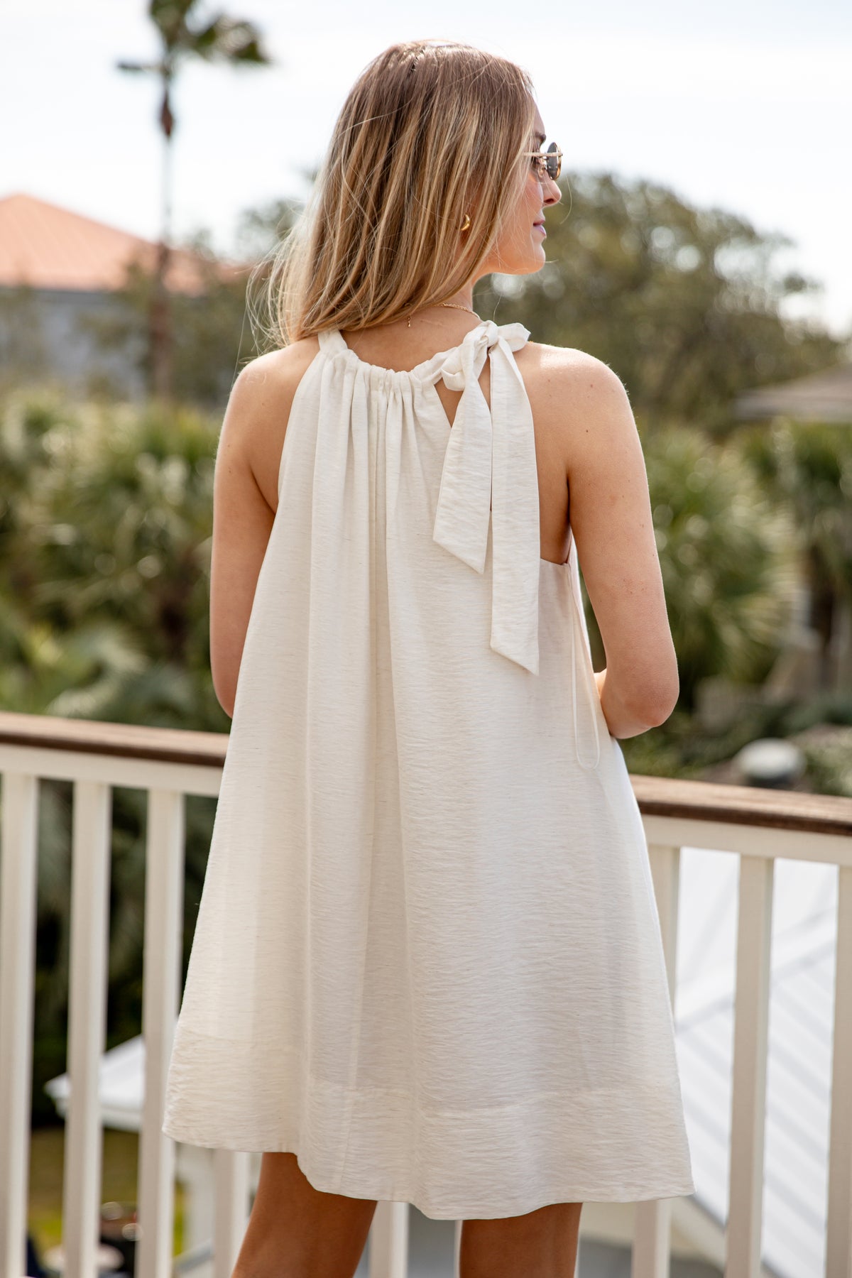 Woman wearing a white dress with a bow detail on a balcony with greenery in the background
