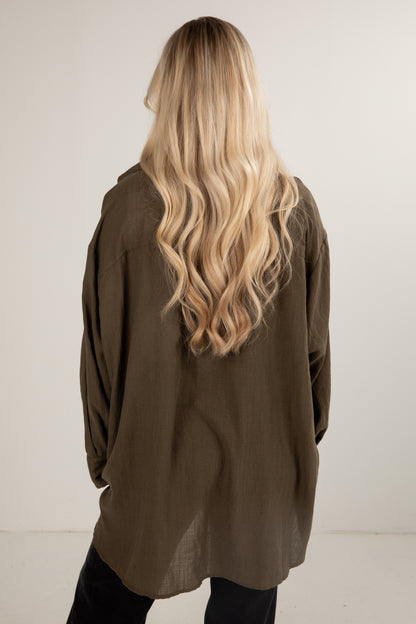 Person wearing an olive green jacket with long blonde hair, standing against a white background