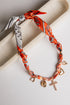 Bracelet with orange patterned bandana wrap and charms on a light background