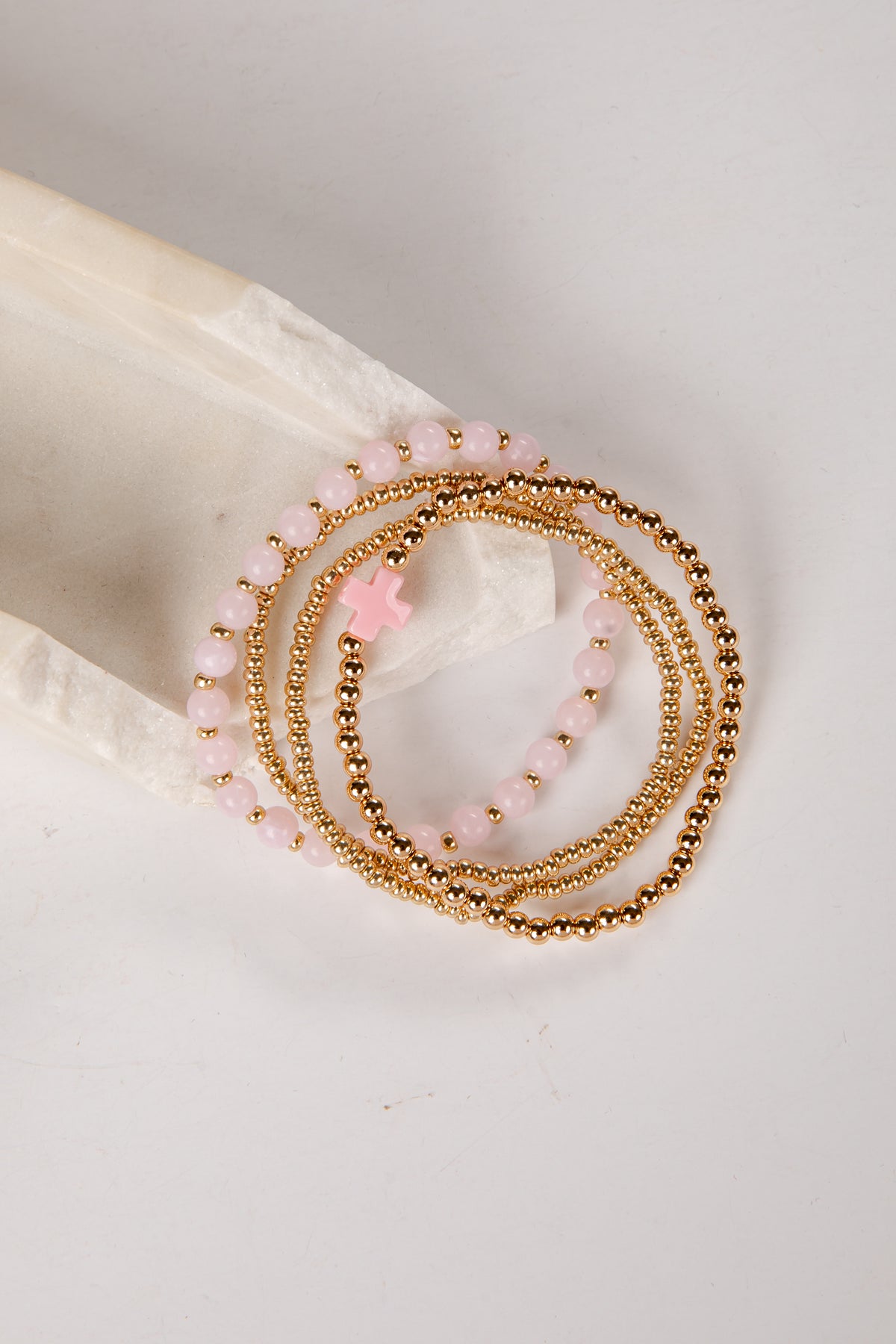 Set of gold and pink beaded bracelets on a white shell