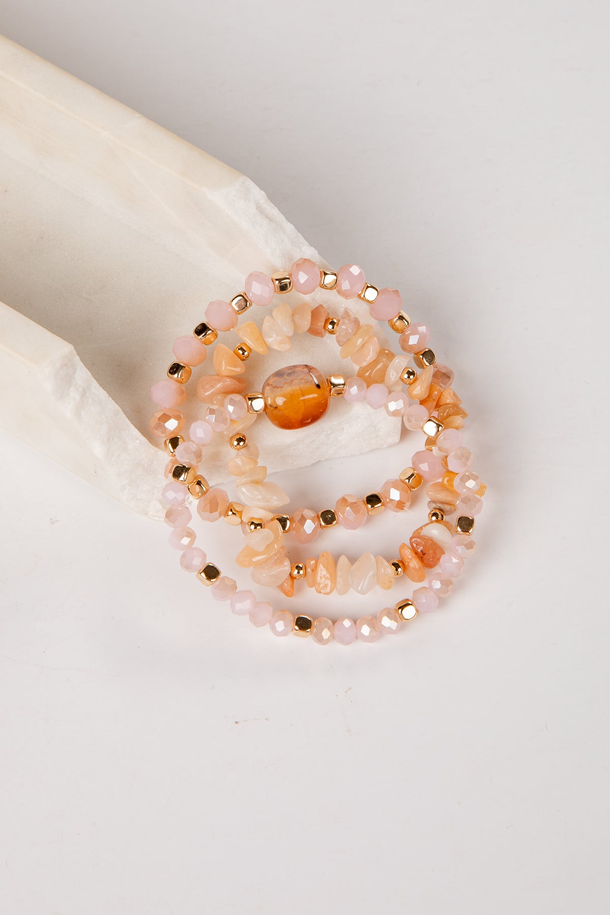 Set of beaded bracelets with peach and gold colors on a white surface