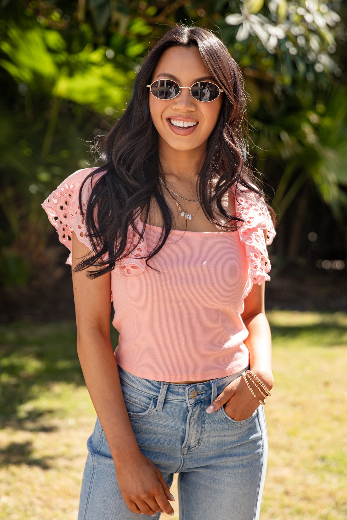 Woman in pink top and denim jeans posing casually outside.