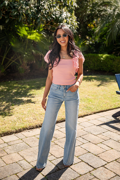 Woman in pink top and denim jeans posing casually outside.