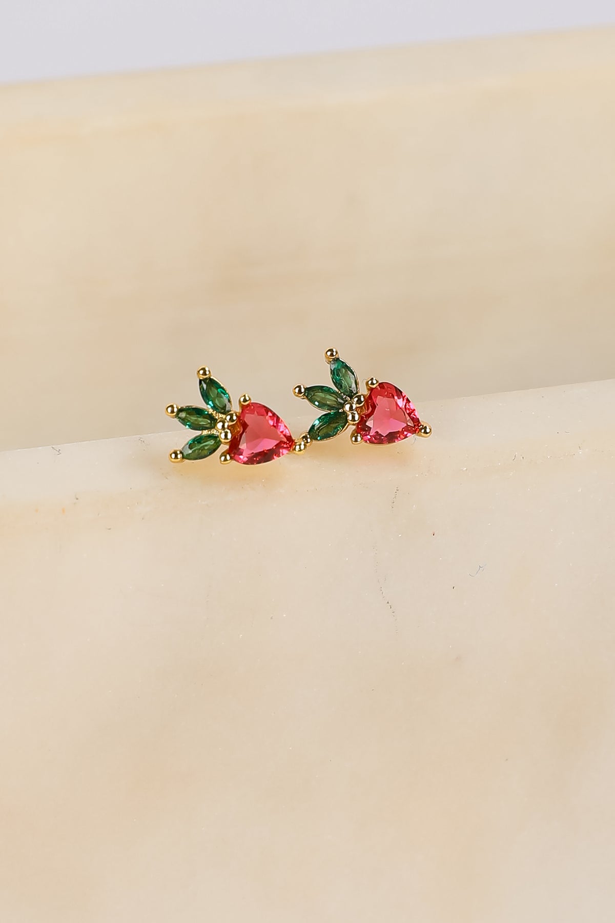 Pair of earrings with heart-shaped gemstones on a beige surface