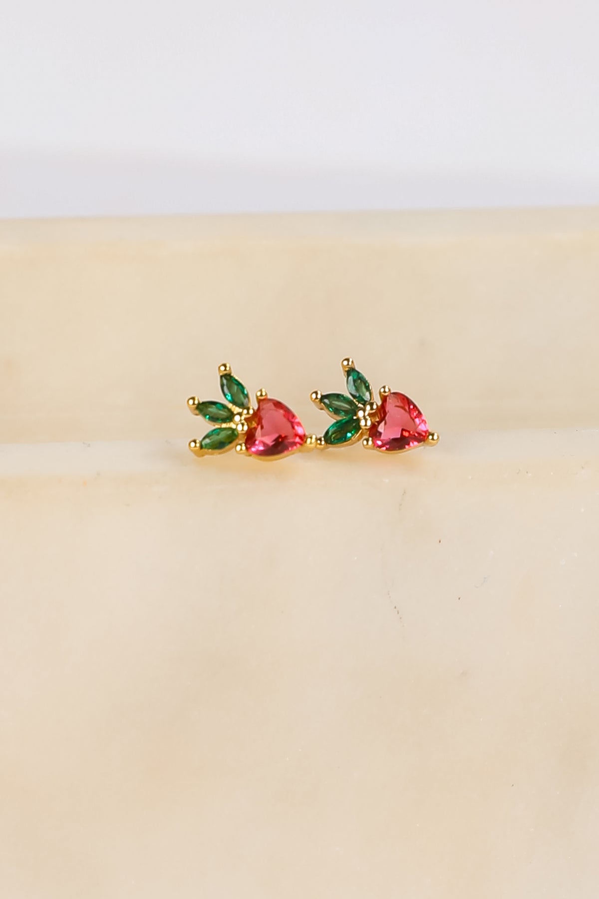 Pair of earrings with red and green gemstones on a beige background