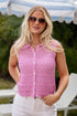 Woman wearing a pink sleeveless top and sunglasses outdoors with lounge chairs and a striped canopy in the background.