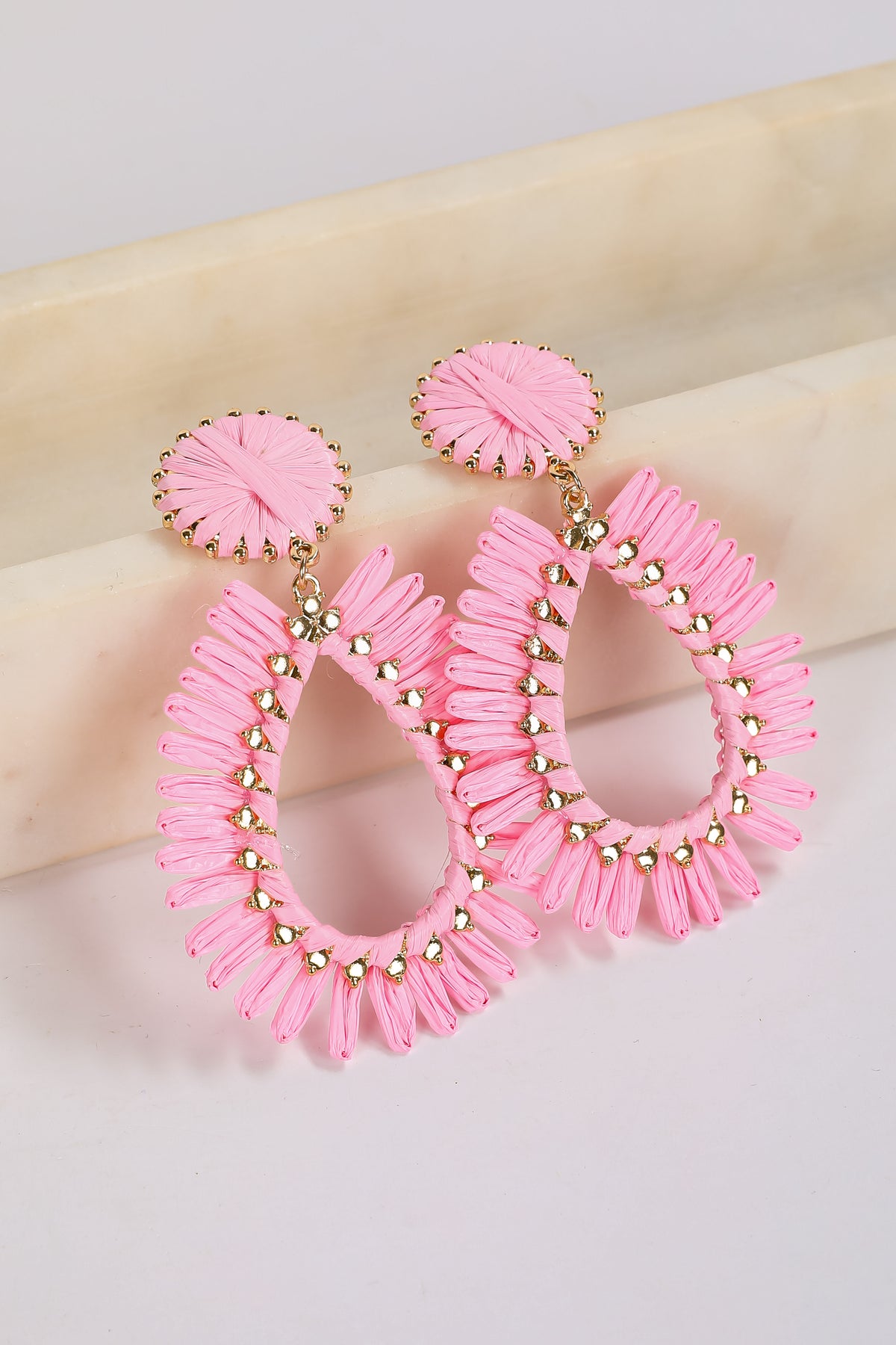 Pink hoop earrings with gold accents on a beige surface
