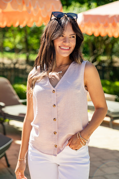 Woman wearing a light pink sleeveless top with gold buttons outdoors under orange umbrellas.