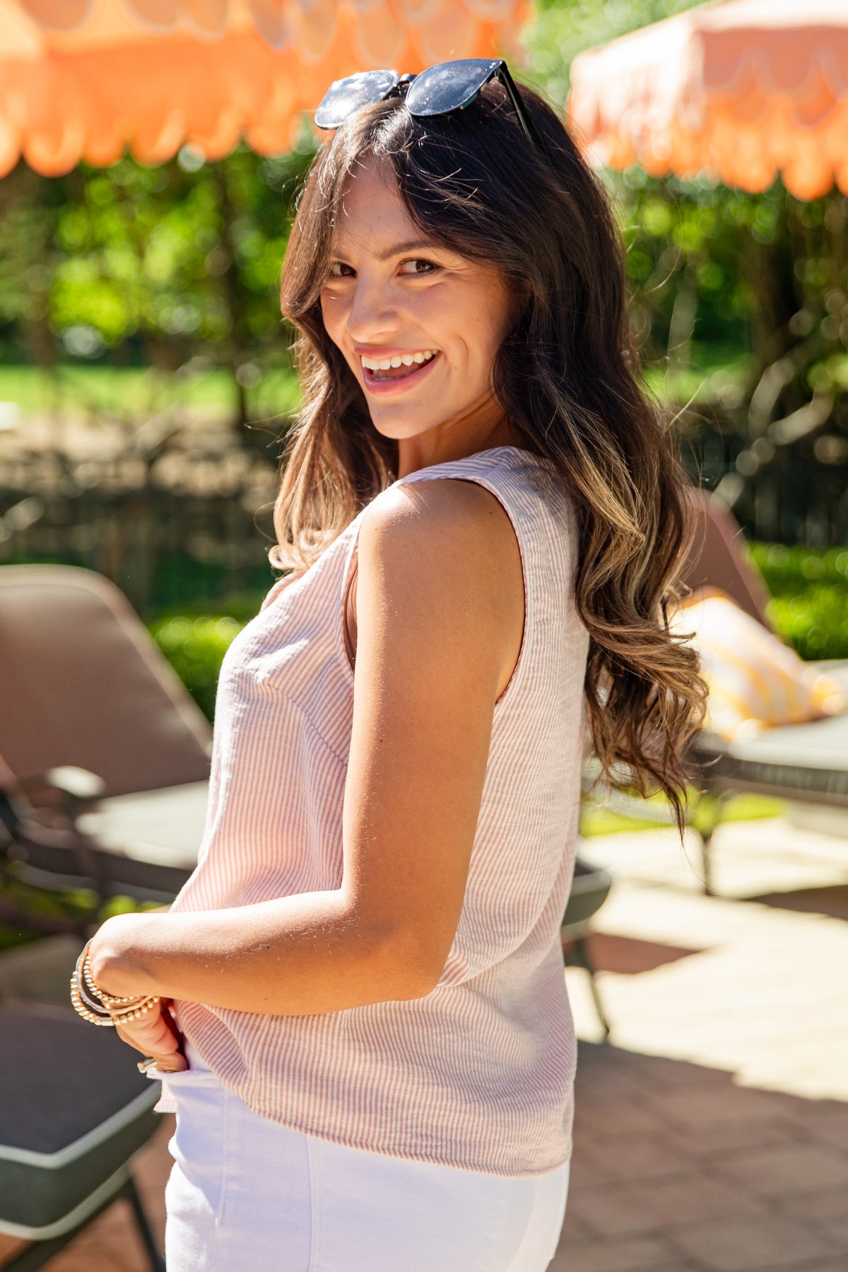 Woman smiling outdoors with orange umbrellas and greenery in the background