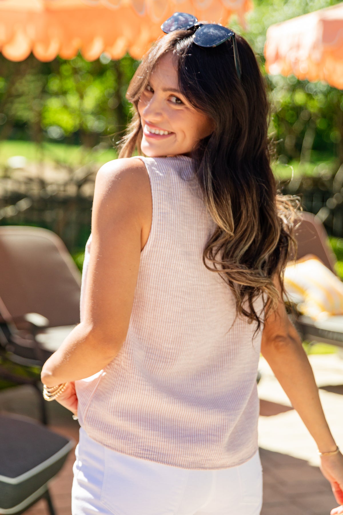 Woman in a light pink sleeveless top and white pants standing outdoors under orange canopies.