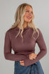 Woman wearing a mauve long-sleeve top against a gray background