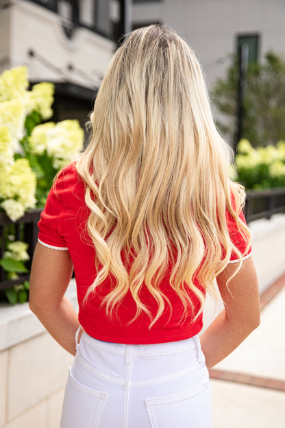 Woman in a red top and white pants standing outdoors with blurred background