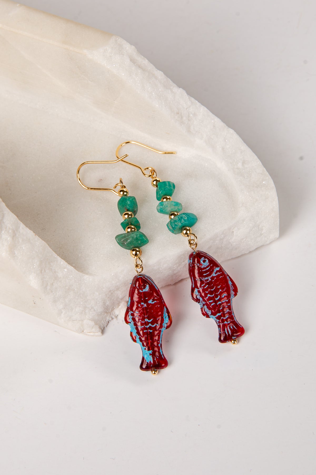 Red fish-shaped earrings with turquoise stones on a white stone background