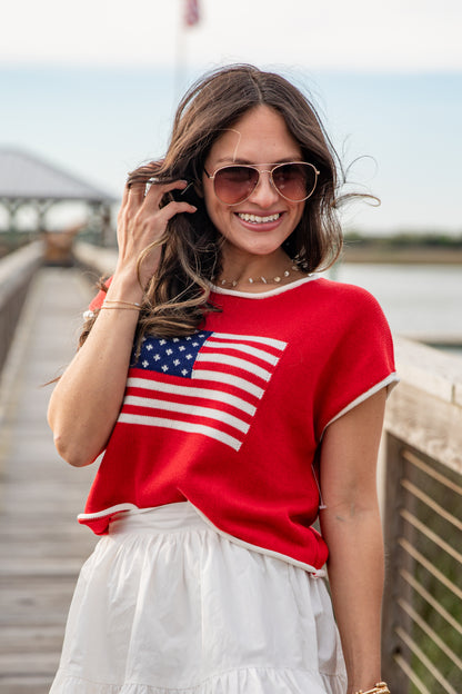 Woman wearing a red shirt with an American flag design, standing on a wooden bridge.