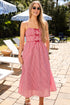Woman in a pink dress standing on a patio with umbrellas and chairs in the background