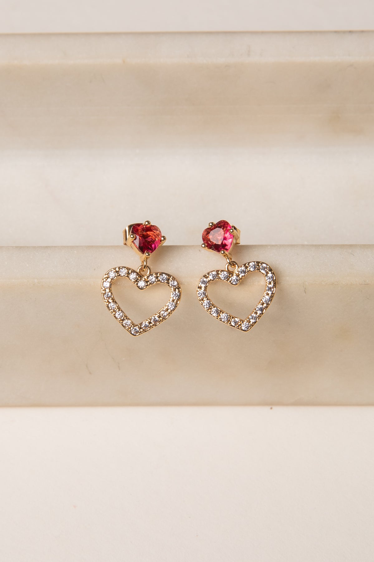 Heart-shaped earrings with red gemstones on a beige background