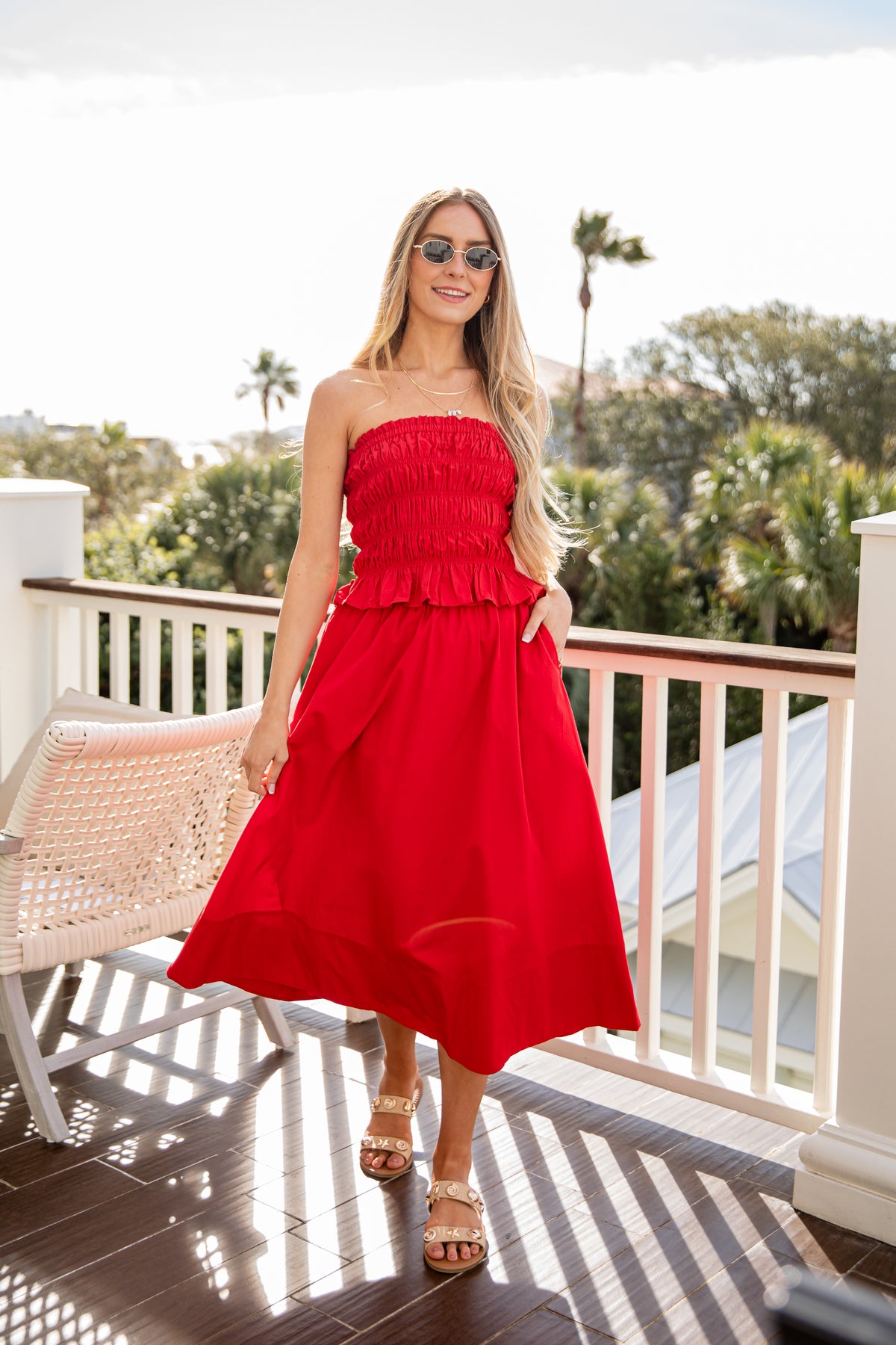 Woman in a red dress standing on a balcony with greenery in the background