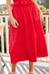 Person wearing a red dress on a balcony with greenery in the background