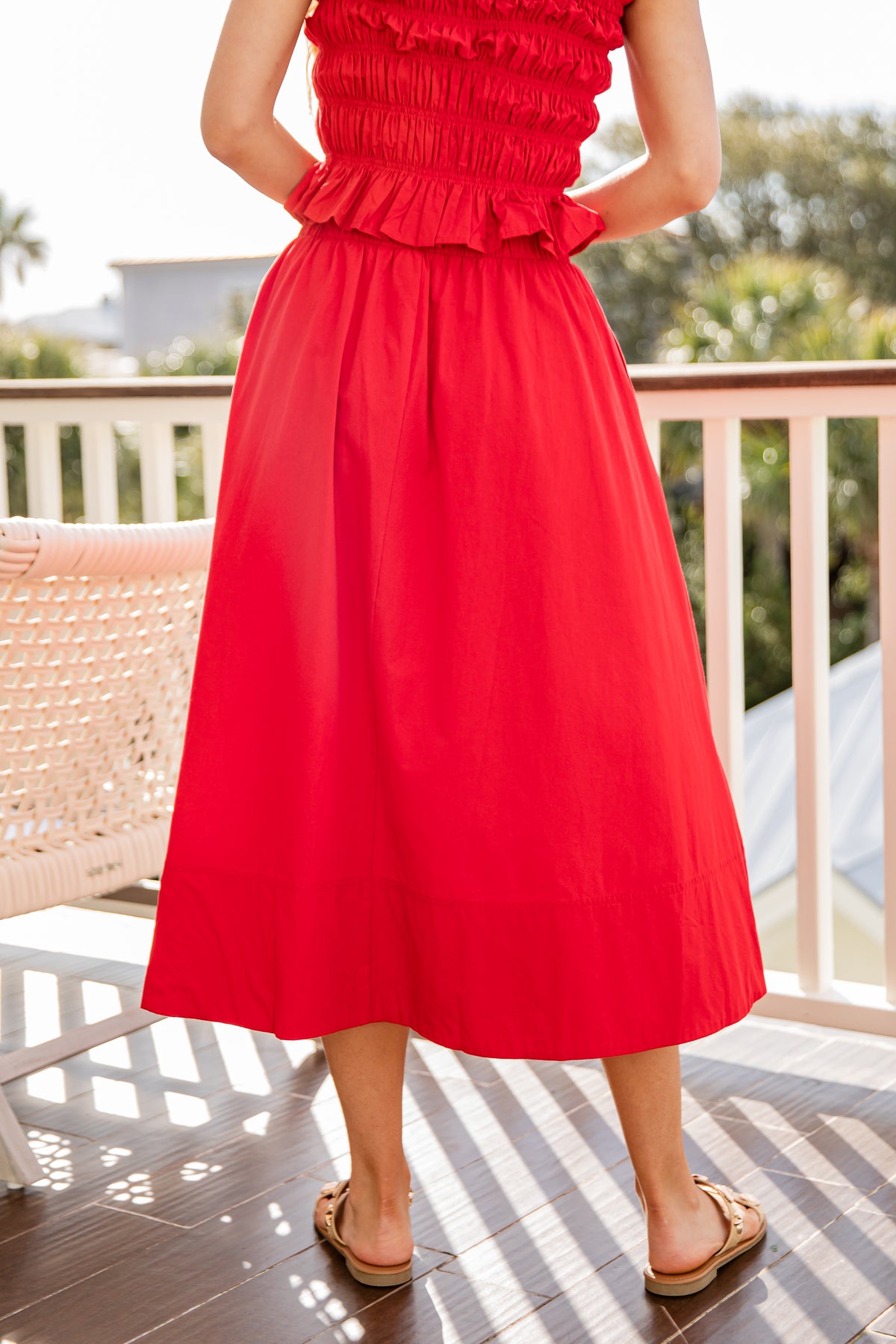 Person wearing a red dress standing on a wooden deck with greenery in the background