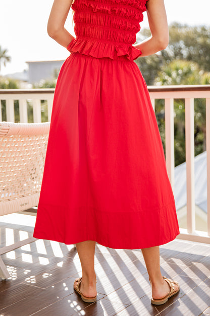 Person wearing a red dress standing on a wooden deck with greenery in the background