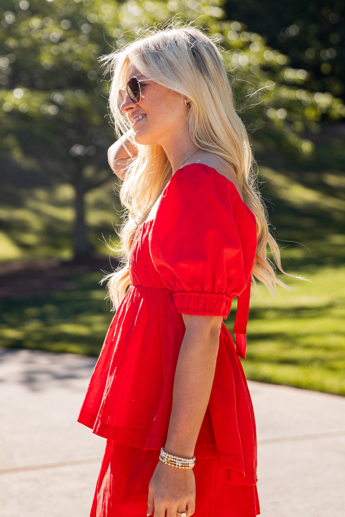 Woman in a red dress standing outdoors with greenery in the background