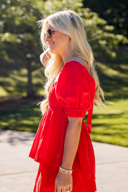 Woman in a red dress standing outdoors with greenery in the background