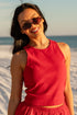 Woman in a red outfit standing on a sandy beach with sunglasses.