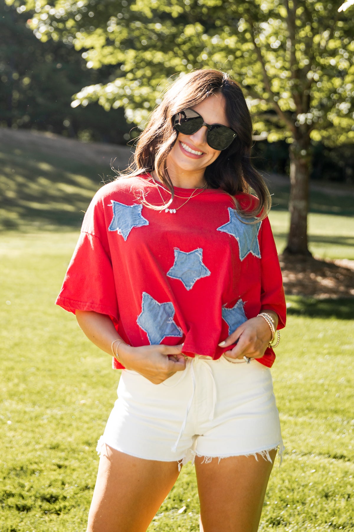 Woman wearing a red shirt with blue stars and white shorts standing in a grassy area.