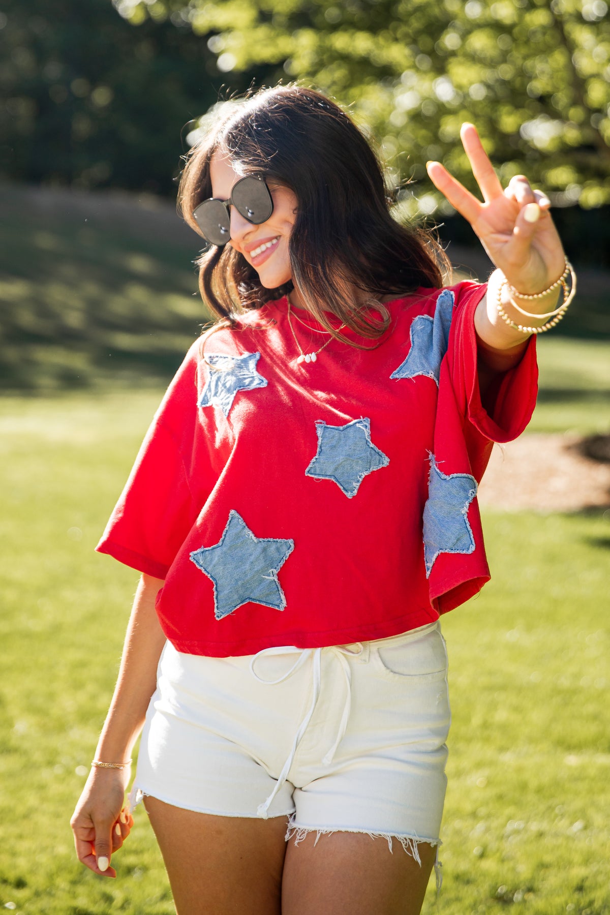 Woman wearing a red shirt with blue star patterns and white shorts, standing outdoors.