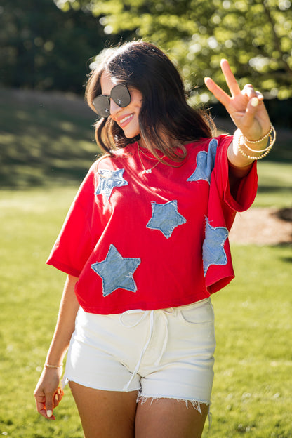 Woman wearing a red shirt with blue star patterns and white shorts, standing outdoors.