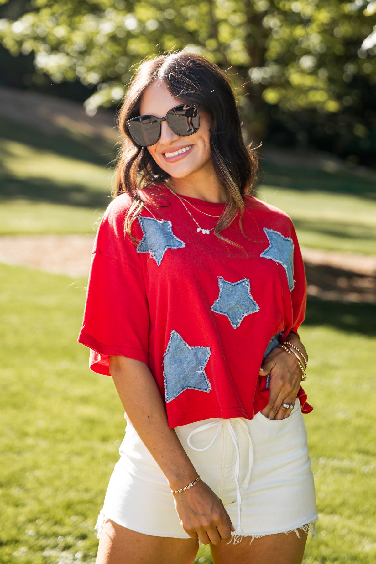 Woman wearing a red sweater with blue star patterns outdoors on a sunny day.
