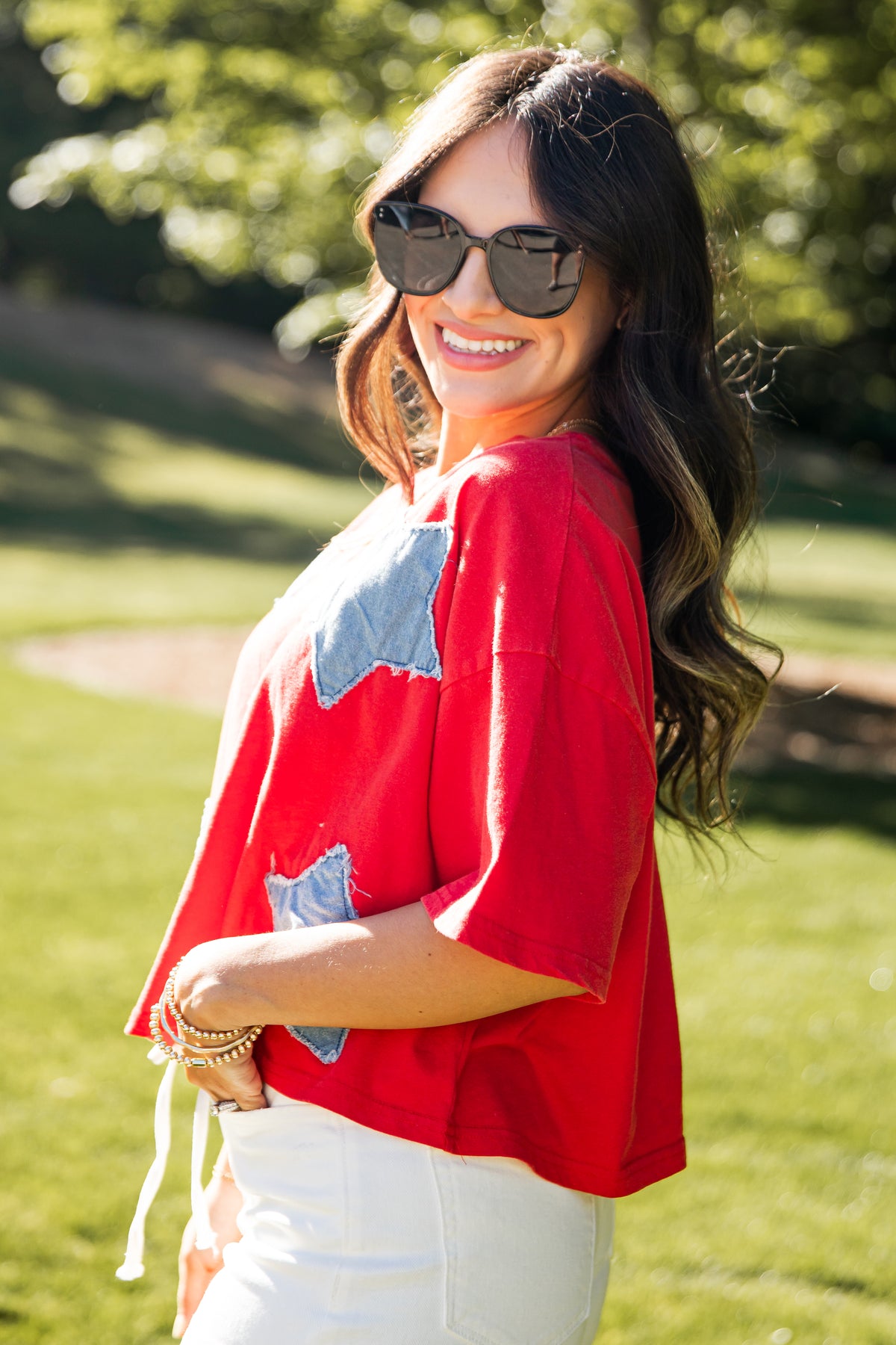 Woman wearing a red top with blue star patterns outdoors on a sunny day.
